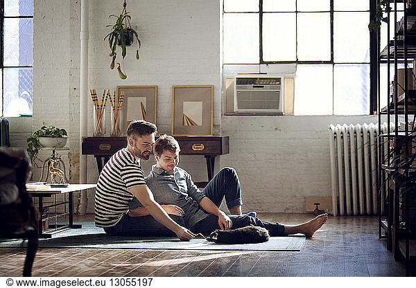 Gay couple looking at cat lying on floor at home