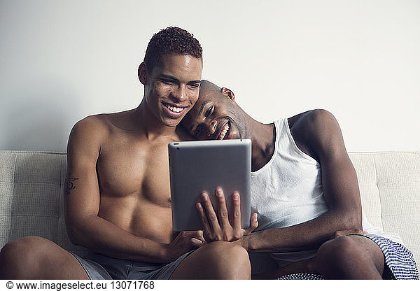Gay couple looking at tablet computer while sitting on sofa
