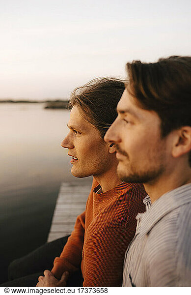 Gay couple looking away while spending leisure time at lakeshore