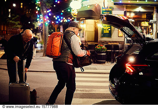 Gay couple putting luggage in car trunk on road in city at night