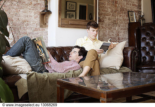 Gay couple reading books while relaxing on sofa at home