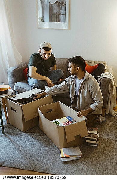 Gay couple talking to each other while unpacking cardboard boxes at home