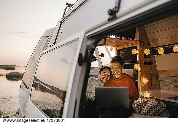 Gay couple using laptop seen through doorway of camping van