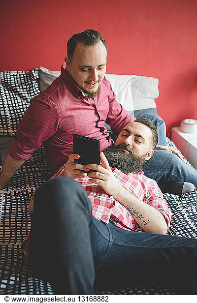 Gay couple using smartphone in bedroom