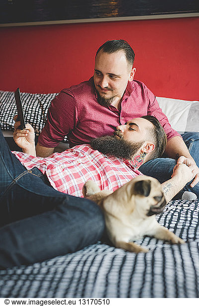 Gay couple with dog  using smartphone in bedroom