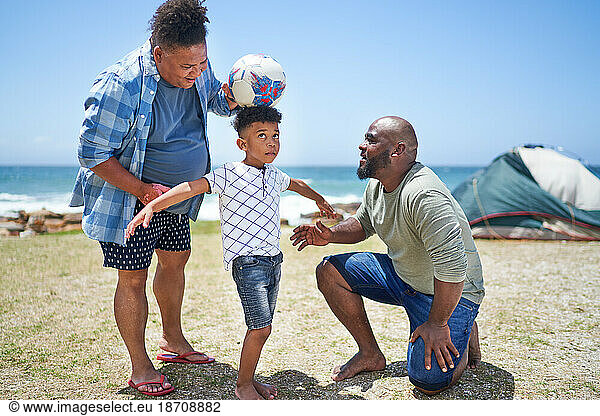 Gay male couple and son playing with soccer ball on sunny beach