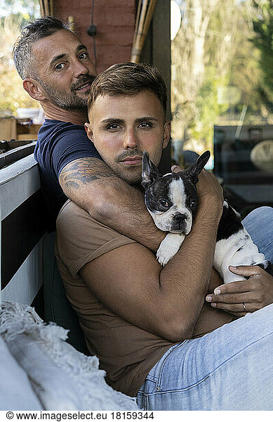 Gay male couple hugging while holding their French Bulldog