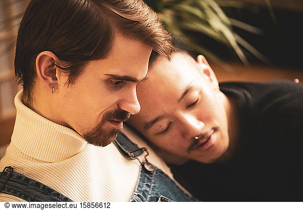 Gay male inter-racial couple cuddle and smile during virus lock down