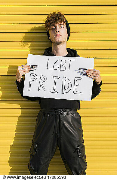 Gay man holding placard in front of yellow shutter