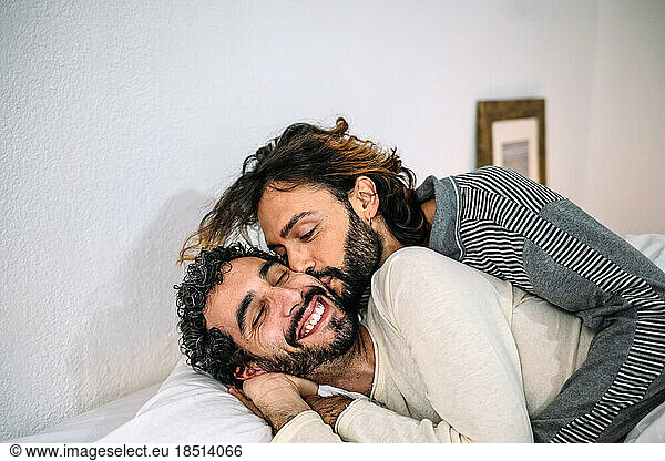 Gay man kissing boyfriend lying on bed at home
