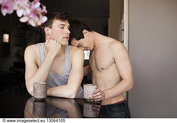 Gay man leaning head on boyfriends shoulder while standing in kitchen