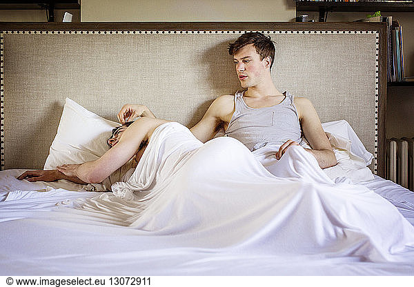 Gay man looking at boyfriend while relaxing in bed at home