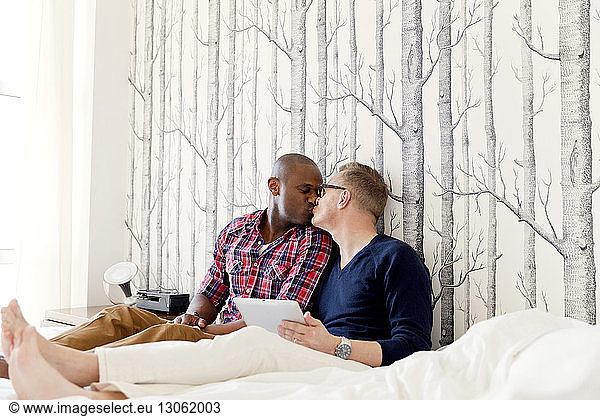 Gay men kissing while resting on bed