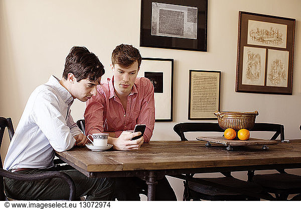 Gay men looking at smart phone while sitting by table