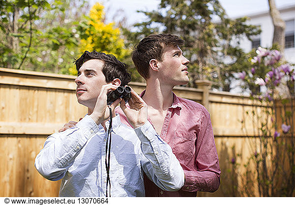 Gay men with binocular looking away while standing in backyard