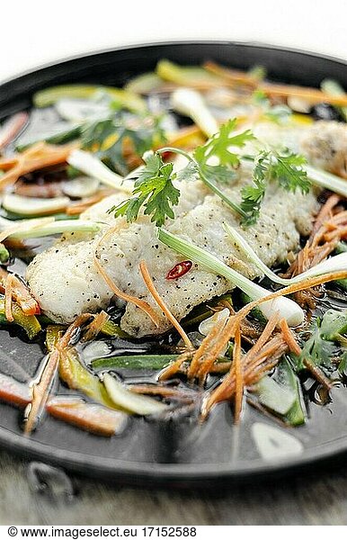 Gedämpftes würziges Fischfilet nach kantonesischer Art mit Gemüse auf einer heißen Platte.