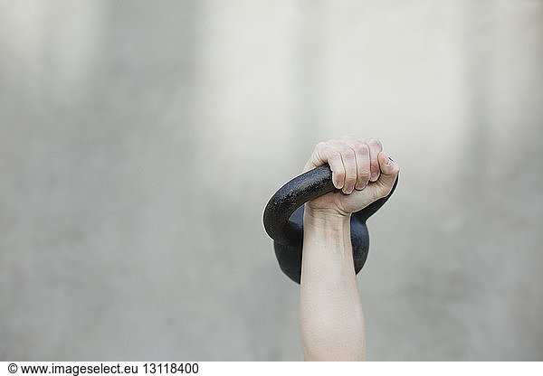Gekrümmte Hand einer Frau  die beim Sport die Kettlebell gegen die Wand hebt