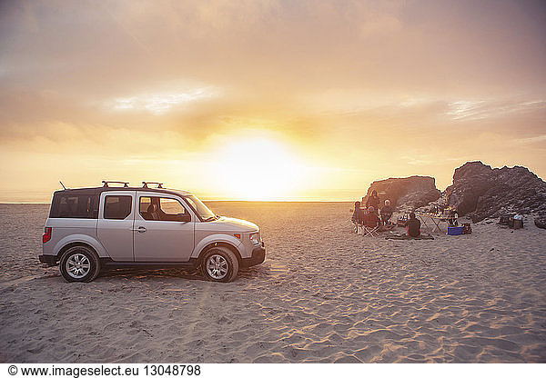 Geländewagen am Strand geparkt  während Freunde bei Sonnenuntergang zelten