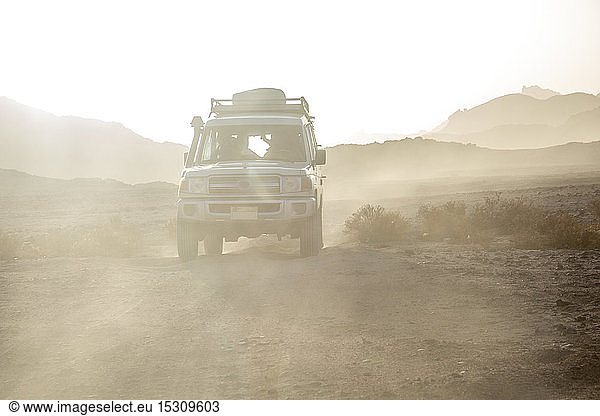 Geländewagen auf unbefestigter Straße inmitten von Staub in der Wüste gegen den Himmel bei Sonnenuntergang
