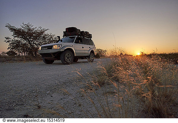 Geländewagen fährt bei Sonnenaufgang auf einer unbefestigten Straße,  Makgadikgadi Pans,  Botswana