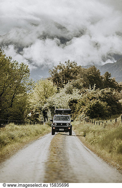 Geländewagen fährt unbefestigte  von Bergen umgebene Straße  Neuseeland