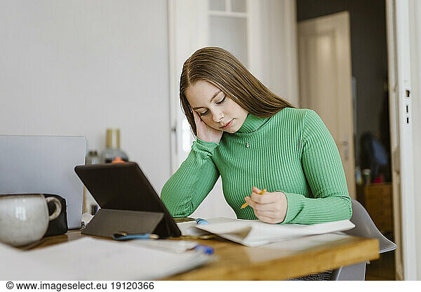 Gelangweilte junge Frau studiert am Tisch