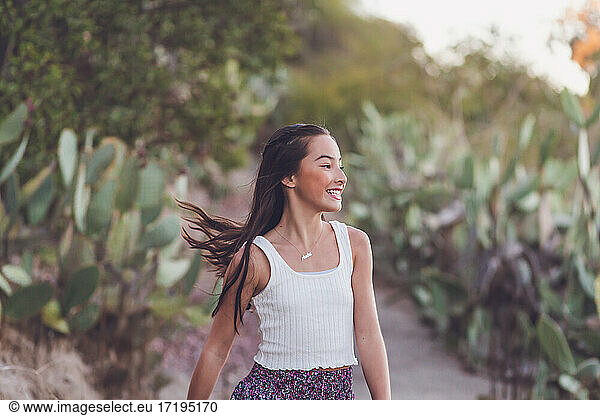 Gemischtrassiges Mädchen  das mit fliegenden langen Haaren über einen Kaktuspfad läuft.