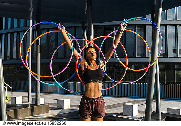 Generation Z young woman holding five Hula Hoop in downtown at sunset