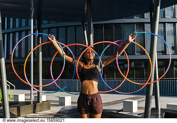 Generation Z young woman holding five Hula Hoop in downtown at sunset