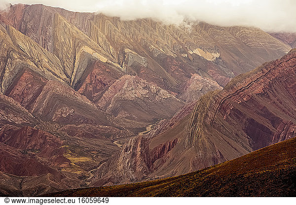 Geologisch interessanter Berg wird von der stürmischen Spättagssonne in rötlichen Tönen beleuchtet; Humahuaca  Jujuy  Argentinien