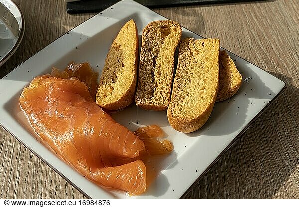 Geräucherte Lachsscheiben mit getoastetem Brot auf einem quadratischen Teller zum Frühstück.