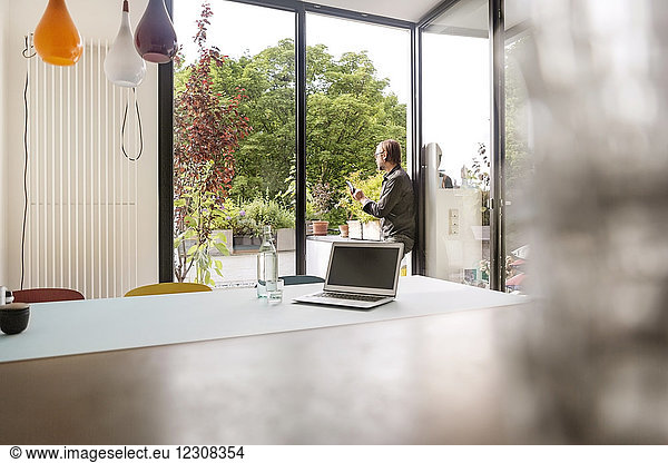 Germany, businessman using tablet on balcony, laptop on table