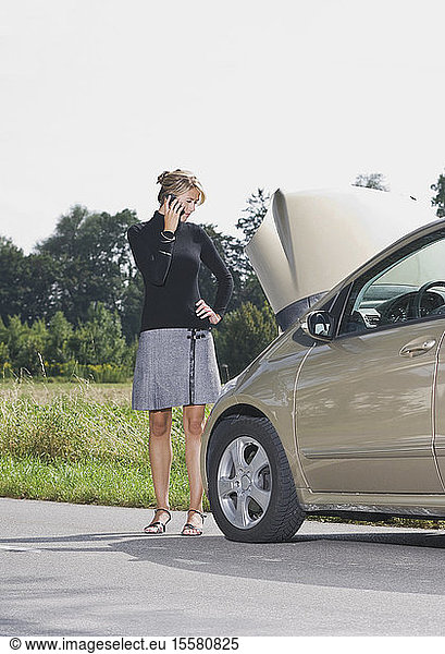 Germany  Augsburg  Young woman standng by car on road using mobile phone