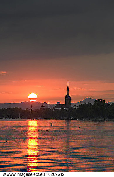 Germany  Baden-Wurttemberg  Radolfzell  Cloudy sky over Lake Constance at moody sunset with tower of Radolfzeller Munster in background
