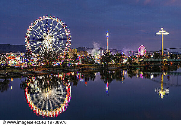 Germany  Baden-Wurttemberg  Stuttgart  Cannstatter Wasen  Glowing Ferris Wheel reflecting in Neckar river at night