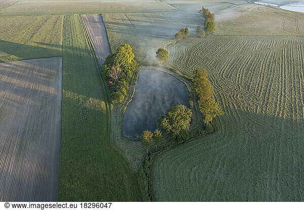 Germany  Bavaria  Aerial view of pond in middle of countryside field at foggy dawn