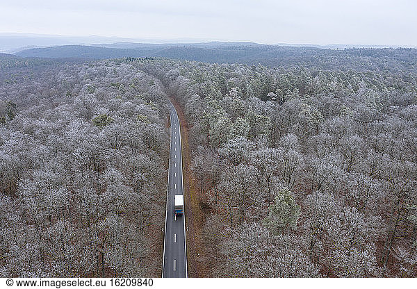 Germany  Bavaria  Drone view of truck driving along asphalt road cutting through Steigerwald forest in winter