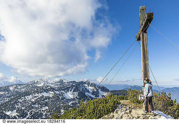 Germany  Bavaria  Female hiker standing beside summit cross on Simetsberg mountain