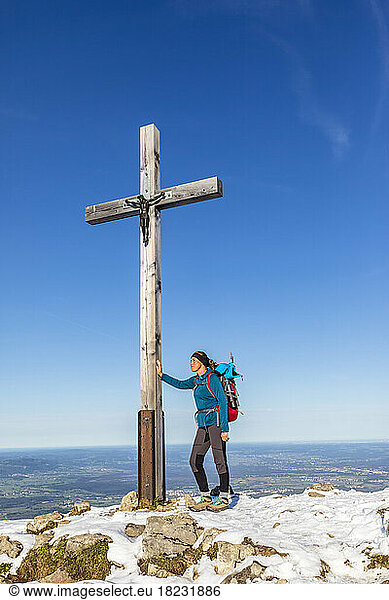 Germany  Bavaria  Female hiker standing in front of summit cross on Hochries mountain