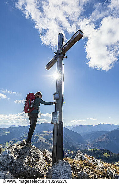 Germany  Bavaria  Female hiker touching summit cross on Kaserwand mountain