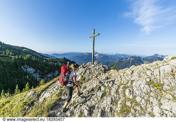 Germany  Bavaria  Female hiker walking past summit cross on Taubenstein mountain