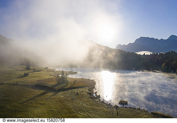 Germany  Bavaria  Krun  Drone view of wafts of fog floating over shore of Geroldsee at sunrise