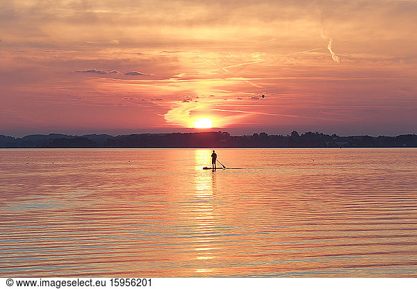 Germany  Bavaria  Lake Chiemsee  Silhouette of person paddleboarding at moody sunset
