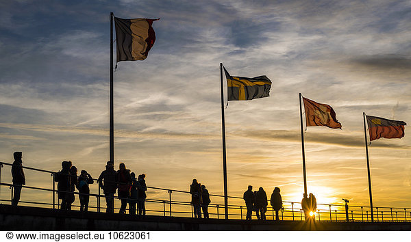 Germany  Bavaria  Lindau  silhouette of people  harbour and flags at sunset