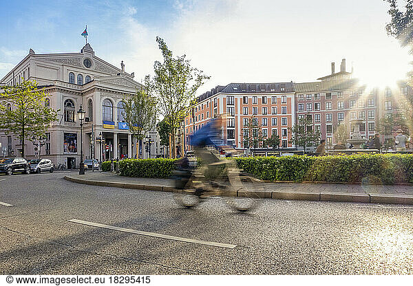 Germany  Bavaria  Munich  Blurred motion of cyclist passing through Gartnerplatz square at sunset