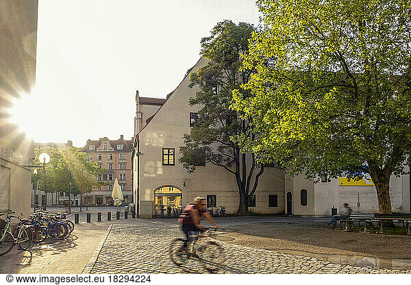 Germany  Bavaria  Munich  Cyclist riding along cobblestone street at sunset