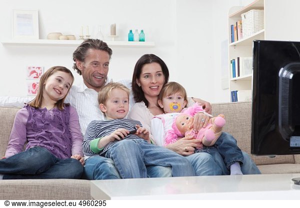 Germany  Bavaria  Munich  Family sitting on sofa and watching TV  smiling