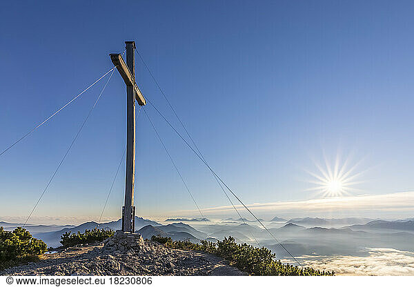Germany  Bavaria  Summit cross of Herzogstand mountain with sun rising in background