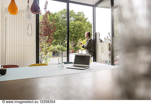 Germany  businessman using tablet on balcony  laptop on table