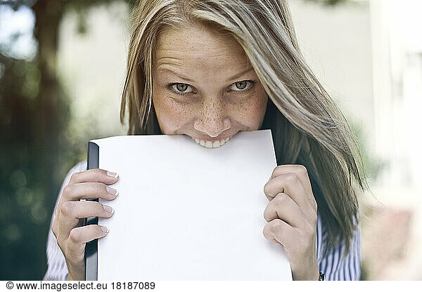 Germany  Duesseldorf  Young woman biting folder  portrait